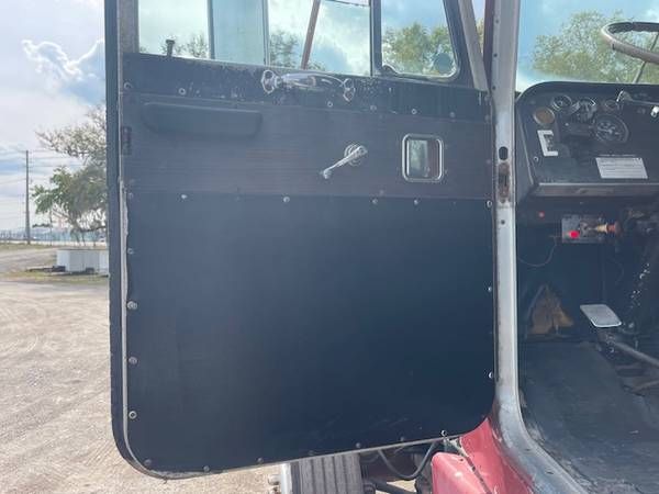 Peterbilt 359 truck door interior with manual window crank and control panel visible in the cab; exterior shows black door panel and riveted edge.