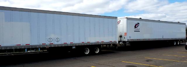 Two white semi trailers connected in a row, parked on a lot under blue sky with scattered clouds.