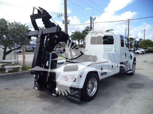 Tow truck with hydraulic tow apparatus at rear, white exterior, cab and long chassis, some chrome wheels, in a parking lot.