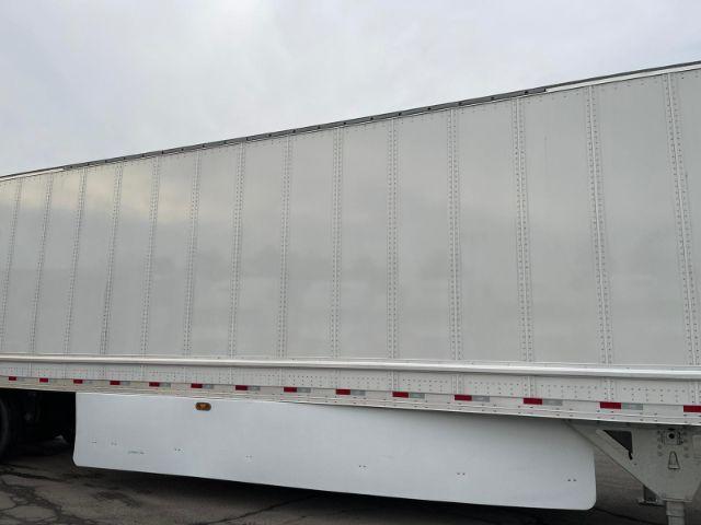 Semi-trailer side view with plain white dry van body and steel frame, no visible branding, wheel area partially visible.