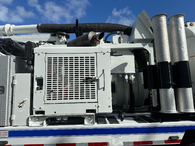 Front view of a Freightliner 114SD vacuum truck showing engine compartment, cooling radiator grille, and vertical exhaust stacks on the side.