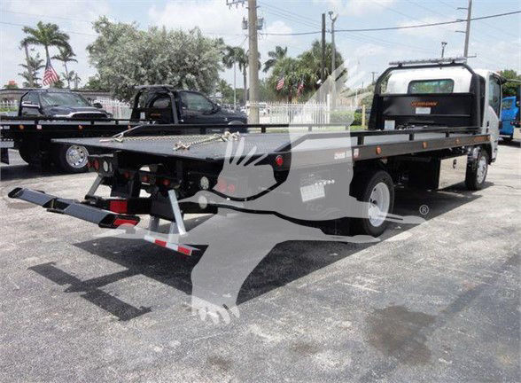 Flatbed tow truck with long steel bed and rear ramps; Isuzu emblem likely on cab; no legible labels visible on the bed in this view.
