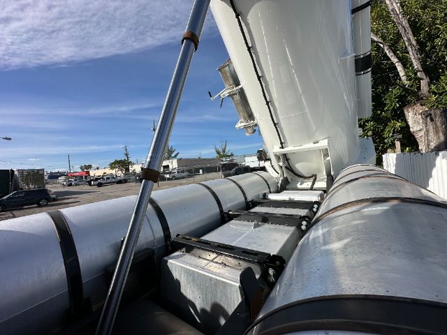 International 7500 vacuum truck with side-mounted tanks and open cab area, showing metallic cylindrical tanks and hydraulic support strut.