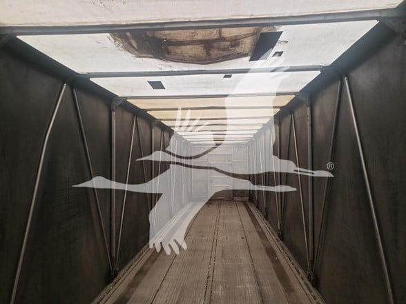 Trailer interior showing metal side rails and open top with wooden floor planks, inside a curtain-side Mac Aluminum flatbed.
