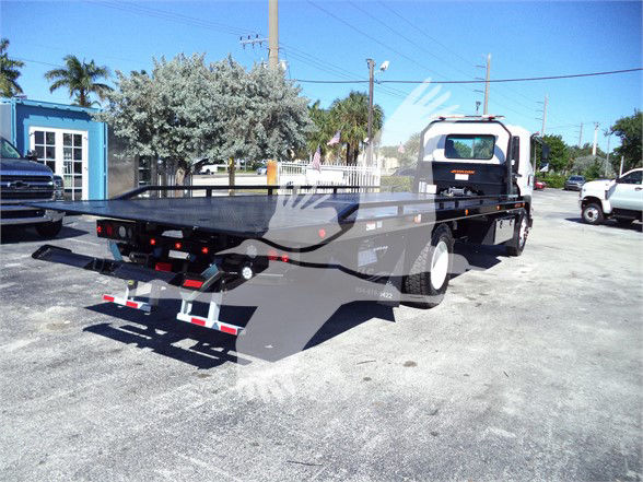 Isuzu FTR tow truck flatbed on lot, side view showing bed and rear lights.