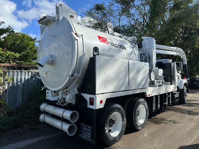 Vacuum truck with large cylindrical tank and rear dual exhaust pipes, Naccon logo on tank, white color, side paneling open compartments, six-wheel chassis.
