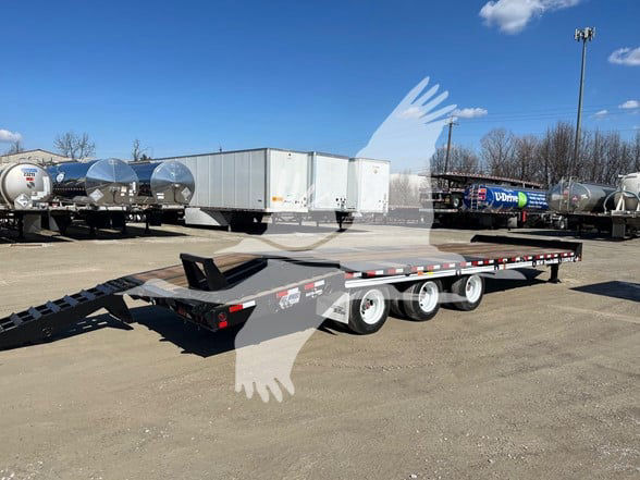Flatbed trailer with three axles and a gooseneck, showing a loading ramp at the rear, in a dealership lot with other trailers and tanks in the background.
