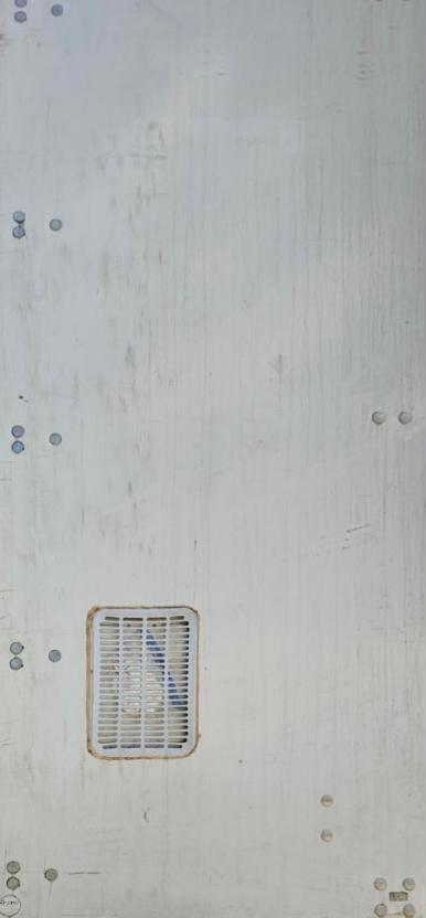 Trailer side panel showing a small air vent grille and minimal hardware, vertical riveted metal surface with light wear.