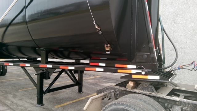 Great Dane 40 ft round bottom dump trailer with black painted tank, undercarriage, and support legs visible. Safety chains and reflective tape along sides.