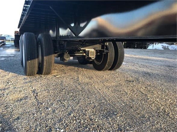 Flatbed trailer underside with dual rear axles and leaf spring suspension showing tires, hubs, and frame components.