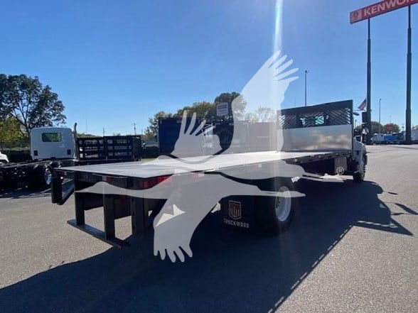 Flatbed truck bed with metal sides and wheel fender, visible text 'TRUCK' on a plate near rear wheel. Large watermark graphic overlay on image.