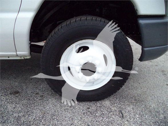Ford E-450 wheel and tire view, front left wheel well, white steel wheel, black tire, part of cargo van body.