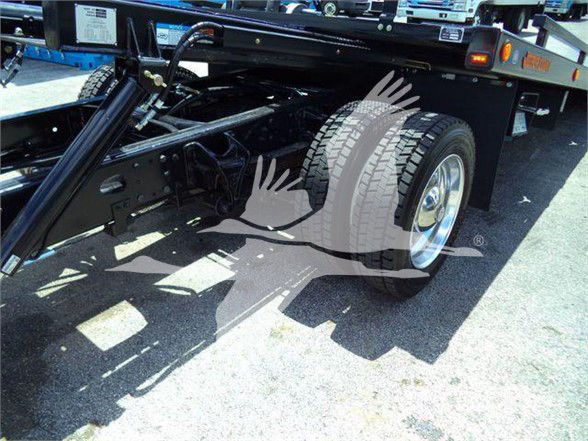Truck chassis and rear wheel area showing flatbed tow equipment and suspension components.