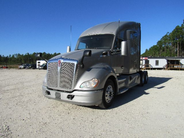 Kenworth T680 sleeper cab semi-truck in a gravel lot, silver/gray color, front grille and bumper visible.