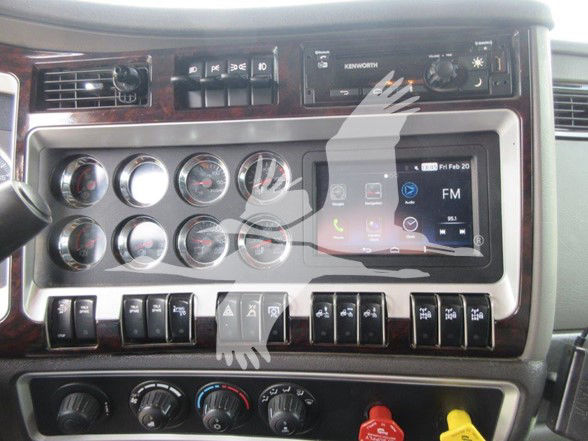 Kenworth W900B truck dashboard with multiple round gauges, switches, Kenworth branding, and a touchscreen display in the center. Visible text includes 'KENWORTH' and various control labels on the panel.