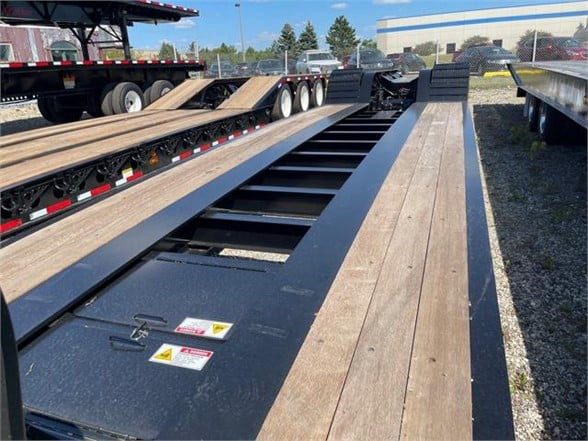 52-foot Fontaine lowboy trailer deck with wooden planks and black steel frame, front cab area visible, warning labels on metal surface.