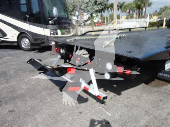 Tow truck or flatbed equipment showing a metal deck with a winch and ramps; visible are chain hooks and a support leg. Some text may be on the vehicle components but not clearly legible.
