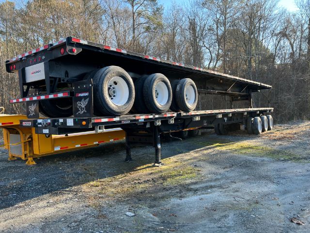 Manac extendable flatbed trailer with triple axles and gooseneck hitch, shown in a yard.