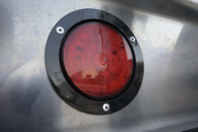 Red circular tail light mounted on aluminum trailer surface with black bezel and three securing screws.