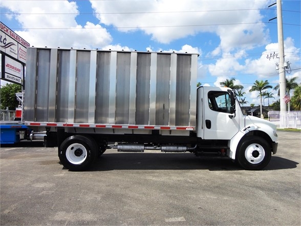 Side view of a Freightliner business class M2 106 dump truck with a tall metallic dumping bed. No visible text on the cab or bed in this shot.