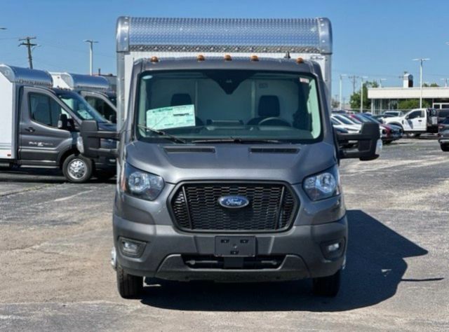 Front view of a 2023 Ford Transit 350 16' box truck with gray body, black grille, and diamond plate top; VIN tag visible through windshield.
