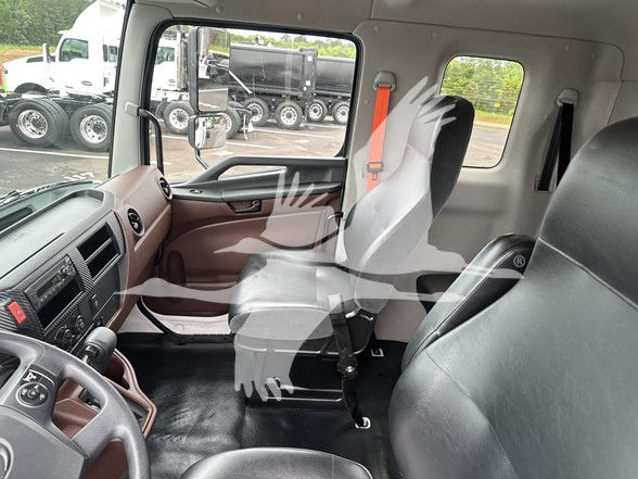 Inside view of a cab and chassis truck with brown and black interior. Front dashboard and steering wheel visible; two seats; seat belts; window and doorway visible.