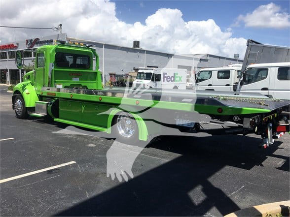 2022 Peterbilt 337 tow truck in green with flatbed, FedEx logo on nearby vehicle, stock number J52310, dealership lot.