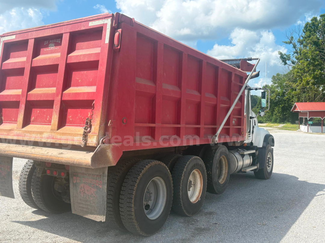 Rear and side view of red dump truck bed on a white Mack CV713 with multiple axles and tires visible.