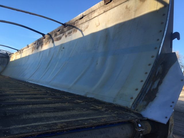 Trailer blade snow plow edge mounted on trailer with bolts along the bottom and hydraulic hoses overhead.