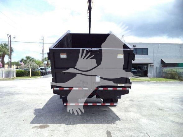 Back of a black dump truck with a grapple body, showing the rear gate and reflective red/white strip. No legible model labels visible from this angle.