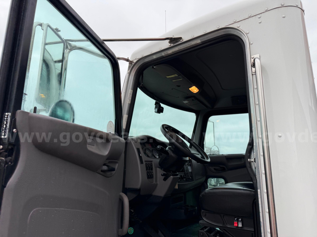 Truck cab interior showing steering wheel and dashboard through driver door opening. Peterbilt Pac-Mac KBF-20H cabin with gray interior, overhead console, and right-hand seat visible.