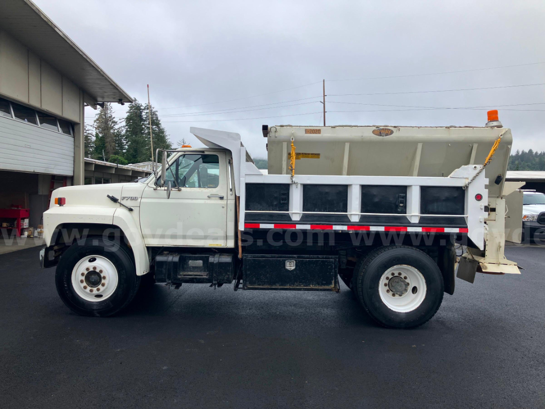 Ford F7000 dump truck side view showing white cab, black dump body, and orange beacon on top of cab.