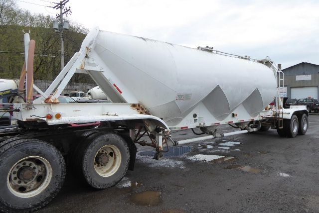 A white Fruehauf pneumatic dry bulk trailer with a tandem-axle rear set and a long cylindrical body. Visible text includes small warning decals on the side near the front of the tank.