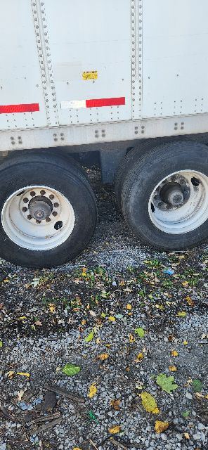 Two trailer wheels and a portion of a white Wabash dry van trailer side with riveted panels and red reflective markings.
