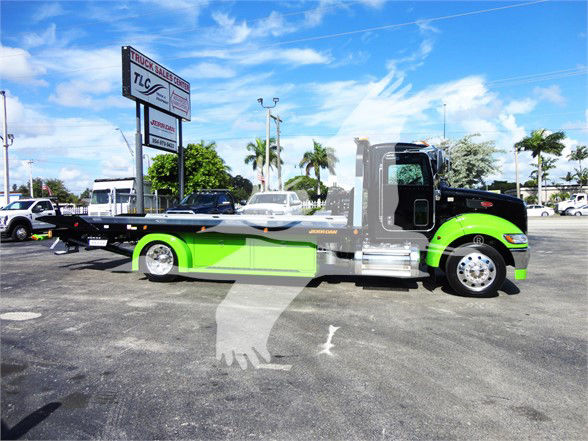 Peterbilt 337 tow truck side view with black and neon green paint, flatbed, showroom lot background.