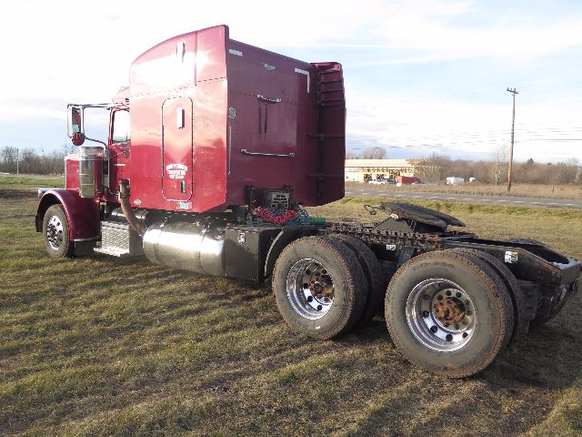 Peterbilt 388 tractor with red cab and dual rear axles, sleeper style, no trailer attached, parked on grass.