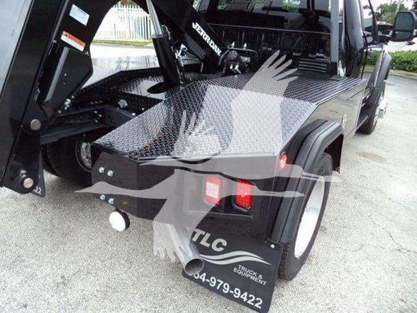 Back view of a 2024 Ford F450 tow truck with diamond plate metal bed and tow equipment, rear wheel and bumper area visible.