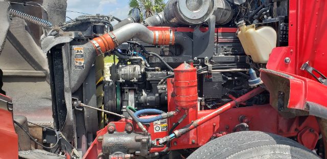 Kenworth TRIAXLE truck engine bay showing radiator, hoses, and red chassis components with visible fuel and fluid lines.