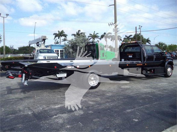 Ford F-750 tow truck with flatbed trailer and black cab on a dealership lot.