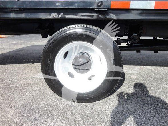 Wheel and tire assembly of a Freightliner Business Class M2 106 flatbed truck, visible underbody and reflection of person taking photo.