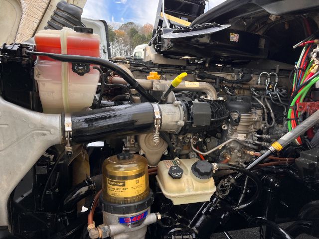 Freightliner Cascadia 125 engine bay showing coolant reservoir, orange and black air intake, oil filter, and various hoses and wires.