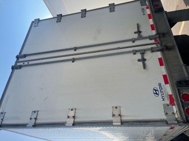 Back of a Hyundai trailer with double rear doors, hinges, latches, and Hyundai logo at lower left; metal frame and reflective red/white strips along the bottom edge.