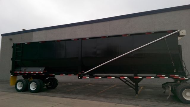 Great Dane dump trailer with black body and round bottom, 40 ft. Dual rear axles, landing legs, and support bar visible; no legible text identified.