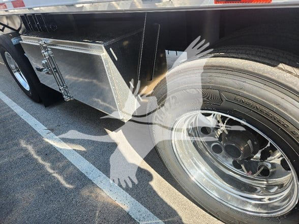 Wabash trailer side view showing chrome wheel, tire, and aluminum toolbox mounted under flatbed.
