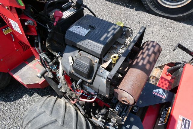 Tractor or agricultural equipment engine bay showing small gasoline engine with air box, alternator, belt, exhaust manifold, and battery.