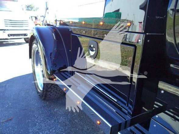 Heavy haul truck fender and side panel with glossy black paint and orange clearance lights along top edge.