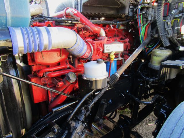 Kenworth T680 engine bay showing red engine, blue intake hose, various hoses, and wiring harness in cab/chassis.