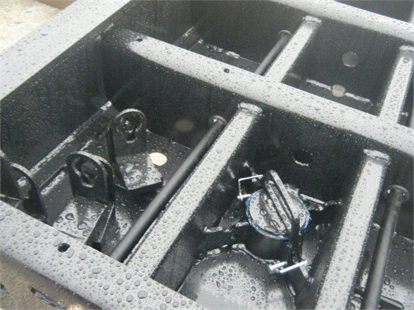 Close-up of a Talbert 55SA flat level deck trailer deck compartments with hydraulic components and hoses visible, rain droplets on metal surfaces.