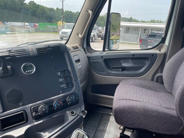 Cab interior of a Freightliner Cascadia showing dashboard controls and passenger seat.