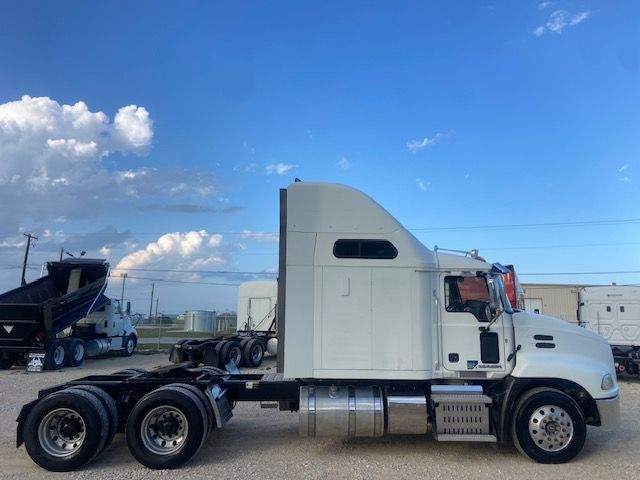 Truck side profile showing 2015 Mack CXU613 sleeper cab with chrome fuel tanks and three rear axles.